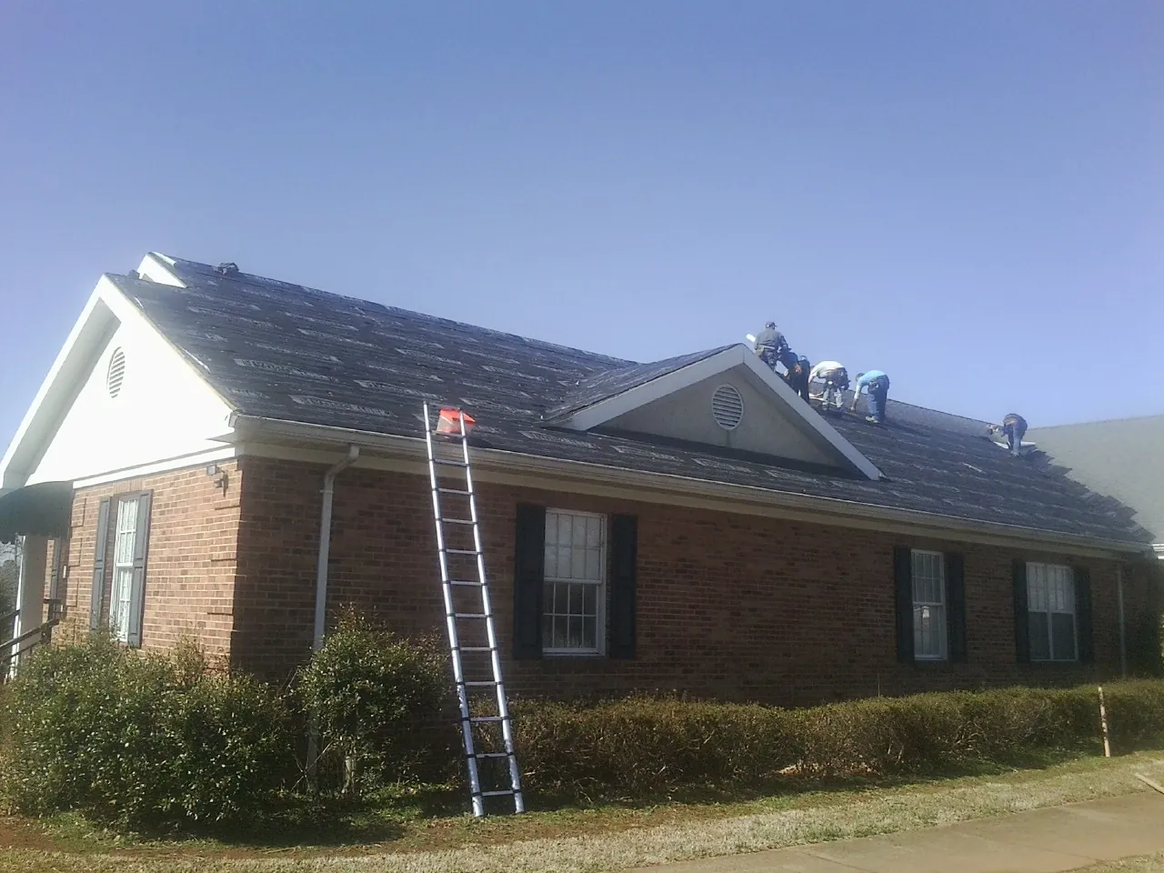 Crew tearing shingles off a brick ranch roof with a ladder set — Emergency Roof Repair work by our crew in Easton