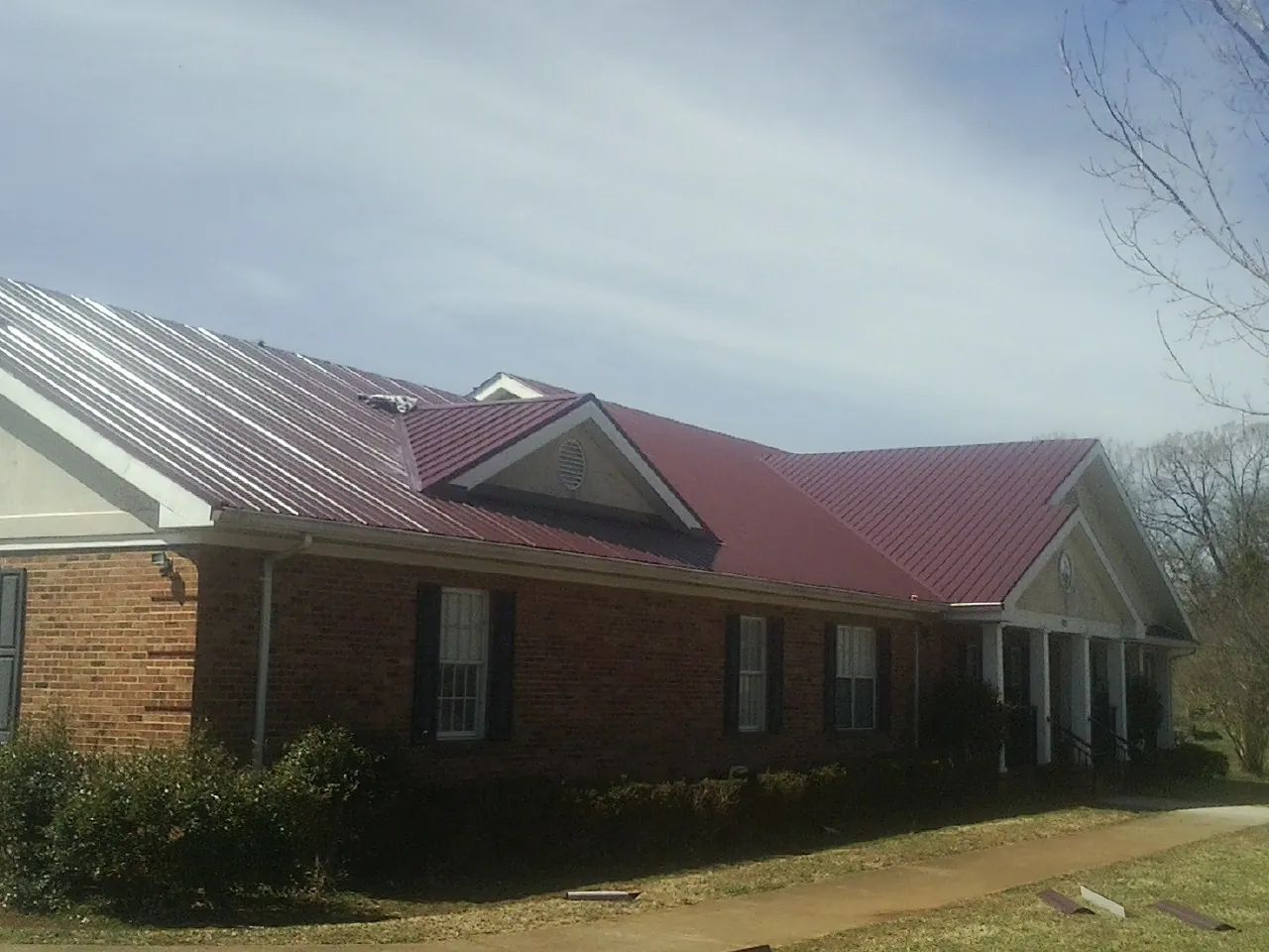 Red metal roof with gabled entries on a long brick building, from a Hail Damage Roof Repair job in Easton