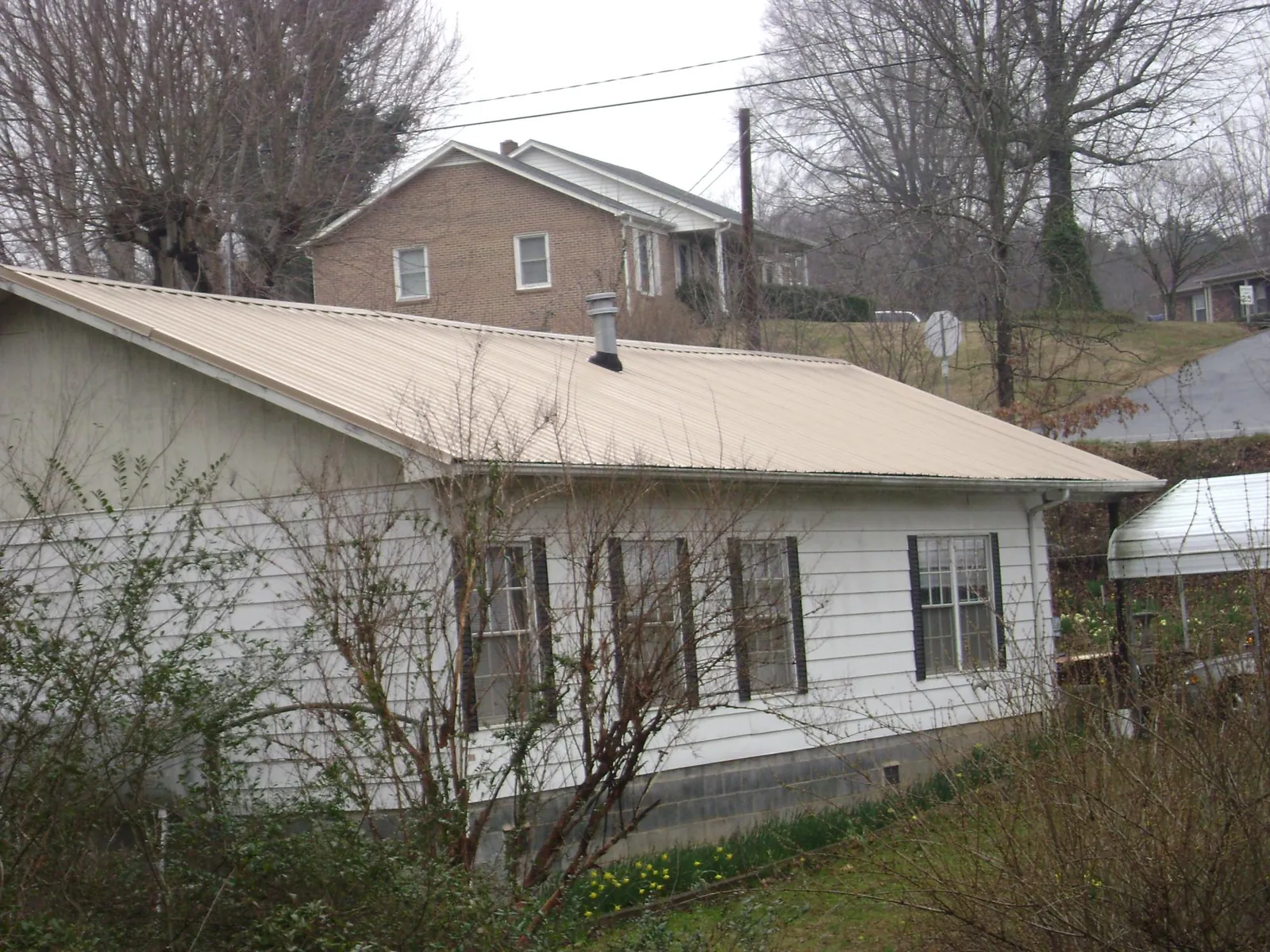 Tan metal roof on a white sided house set into a hillside — Commercial Roofing by Roofing Brothers in Easton